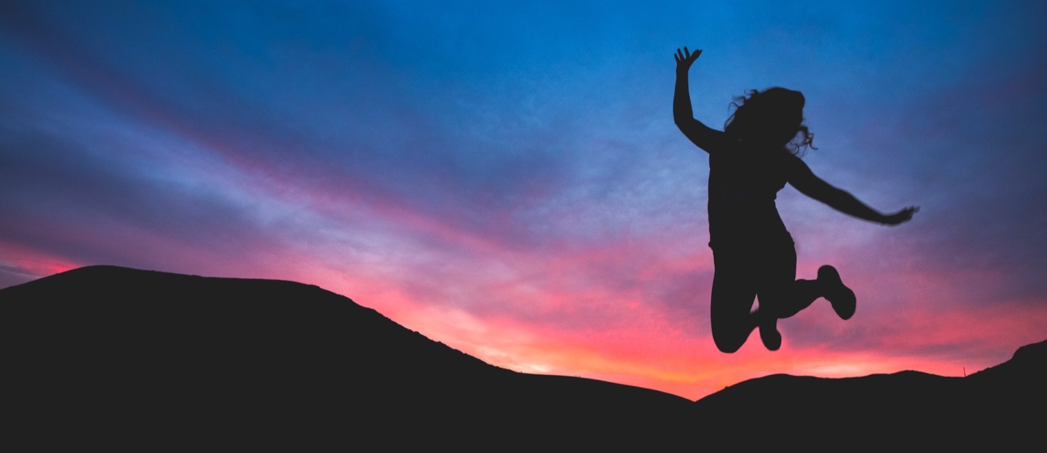 Girl jumping in front of sunset over mountains